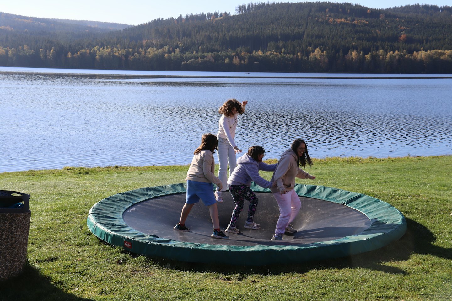 Four children jump on a backyard trampoline by a lake.