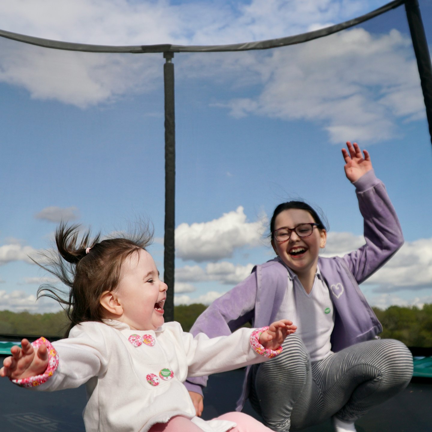 Two happy girls jumping high on a trampoline outdoors.